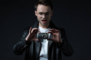 Motosiklet ceketli, şok edici, vahşi adam, siyah kamerada izole bir şekilde fotoğraf çekiyor.