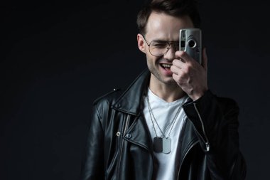 Motosiklet ceketli mutlu stil sahibi vahşi adam siyah kameraya izole edilmiş bir şekilde fotoğraf çekiyor.