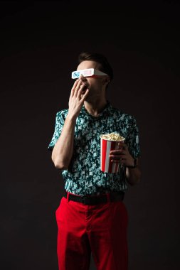 fashionable man in 3d glasses with open mouth in blue colorful shirt and red pants holding popcorn isolated on black clipart