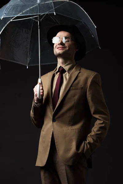 ベージュのスーツを着たエレガントな男の笑顔黒に隔離された帽子と眼鏡を保持傘 — ストック写真
