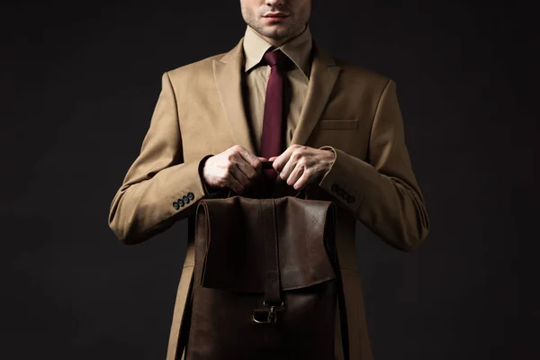 黒で隔離された茶色の革のバックパックを保持ベージュのスーツでエレガントな男のクロップドビュー — ストック写真