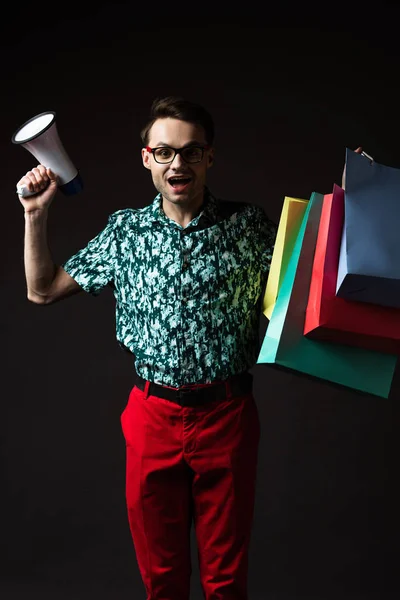 戴眼镜的时髦男人 蓝色五颜六色的衬衫 红色裤子 购物袋和扩音器与黑色隔离 — 图库照片