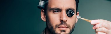 Selective focus of watchmaker in eyeglass loupe holding watch part, panoramic shot clipart