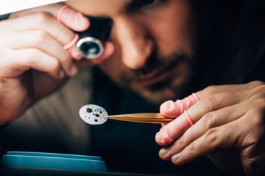 Selective focus of watchmaker holding eyeglass loupe and watch part in tweezers  clipart