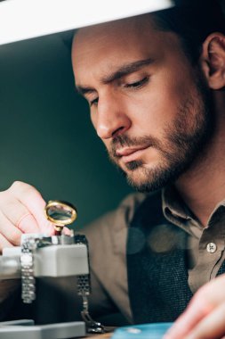Hareket tutucu üzerinde büyüteç ve kol saati ile çalışan yakışıklı bir saatçinin seçici odağı