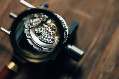 Selective focus of parts of mechanical wristwatch in magnifying glass on table clipart