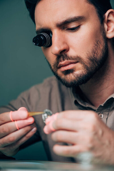 Selective focus of handsome watchmaker working with watch part 