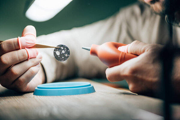 Cropped view of watchmaker cleaning watch part with blower at working table