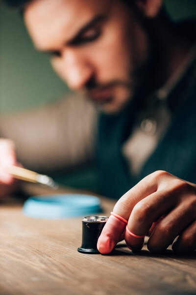 Selective focus of watchmaker holding eyeglass loupe while working at table