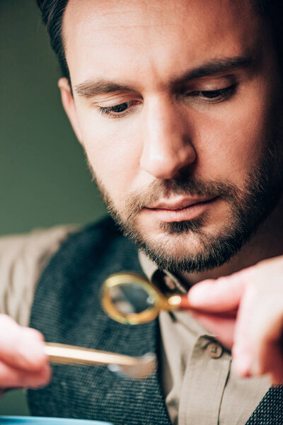 Selective focus of handsome watchmaker holding magnifying glass and watch part 