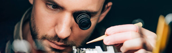 Panoramic shot of watchmaker in eyeglass loupe working with wristwatch isolated on black