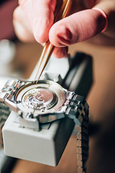 Close up view of watchmaker repairing mechanical wristwatch on movement holder