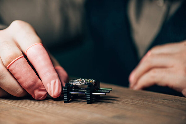 Cropped view of watchmaker in latex fingertips holding watch on movement holder at table