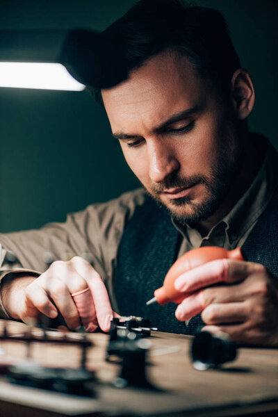 Selective focus of watchmaker cleaning wristwatch with blower at working table