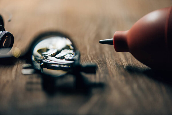 Selective focus of wristwatch, magnifying glass and blower on wooden table