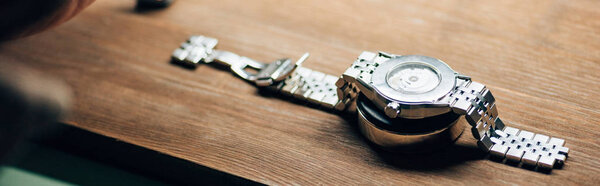 Panoramic shot of wristwatch on stand on wooden table 