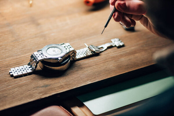 Cropped view of watchmaker working with screwdriver and wristwatch on stand on table