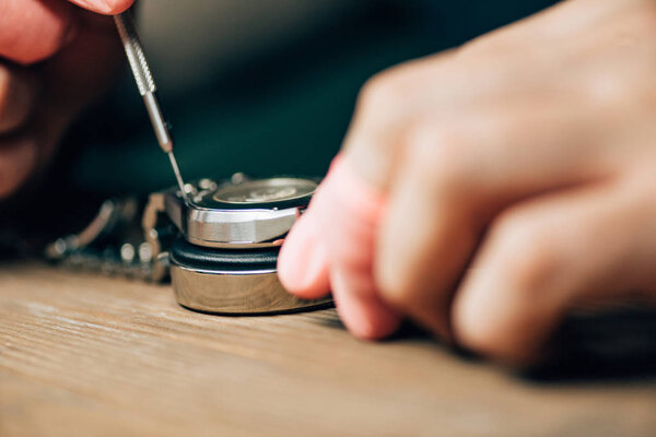 Selective focus of watchmaker using screwdriver for wristwatch on stand on table