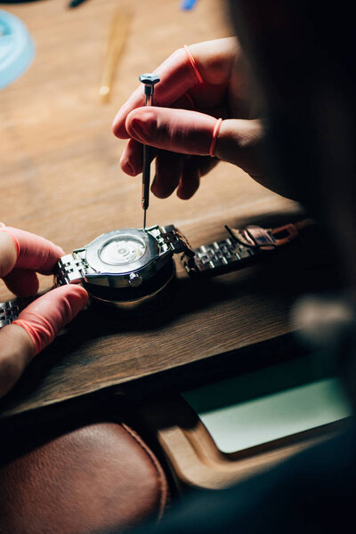 Selective focus of clockmaker repairing wristwatch with screwdriver at table
