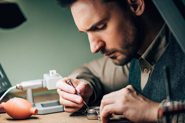 Side view of watchmaker working with screwdriver and wristwatch by equipment on table