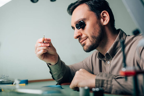 Side view of watchmaker holding watch part in tweezers at working table