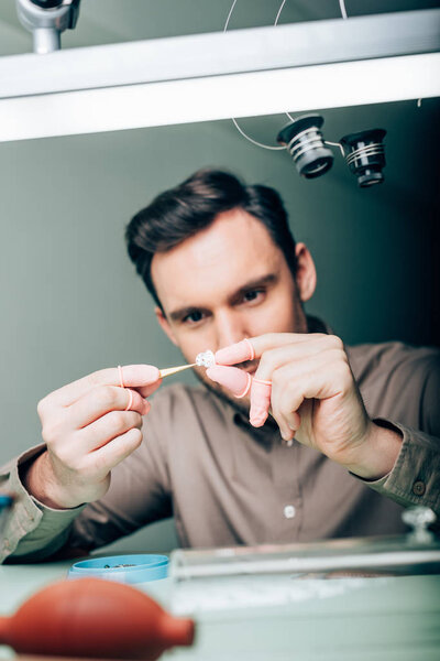 Selective focus of watchmaker working with watch part by equipment on table 