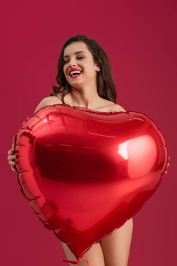 Seksi kız, gözleri kapalı gülümserken elinde kırmızı üzerine izole edilmiş büyük kalp şeklinde bir balon tutuyor.