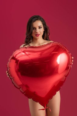 Seksi kız kameraya gülümserken elinde büyük bir kalp şeklinde balon, kırmızıda izole edilmiş.
