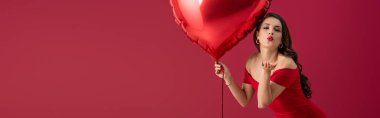 Kalp şeklinde balon tutan ve kırmızı ışıkta izole edilmiş kameraya hava öpücüğü yollayan baştan çıkarıcı, zarif bir kız görüntüsü.