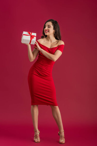 sensual, elegant girl smiling while holding gift box on red background