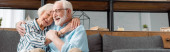Panoramatický záběr usměvavé starší ženy objímající manžela na gauči doma