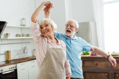 Selective focus of smiling senior couple dancing in kitchen clipart