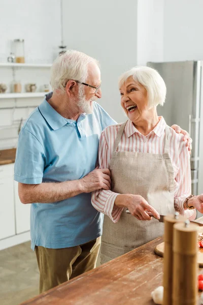 老年男子在厨房桌上做饭时拥抱微笑女人的选择性焦点 — 图库照片
