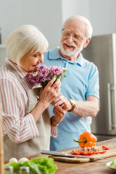 Selective Focus Senior Man Giving Bouquet Wife Fresh Vegetables Kitchen — 스톡 사진