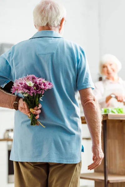 Selective Focus Senior Man Hiding Floral Bouquet While Smiling Wife — 스톡 사진