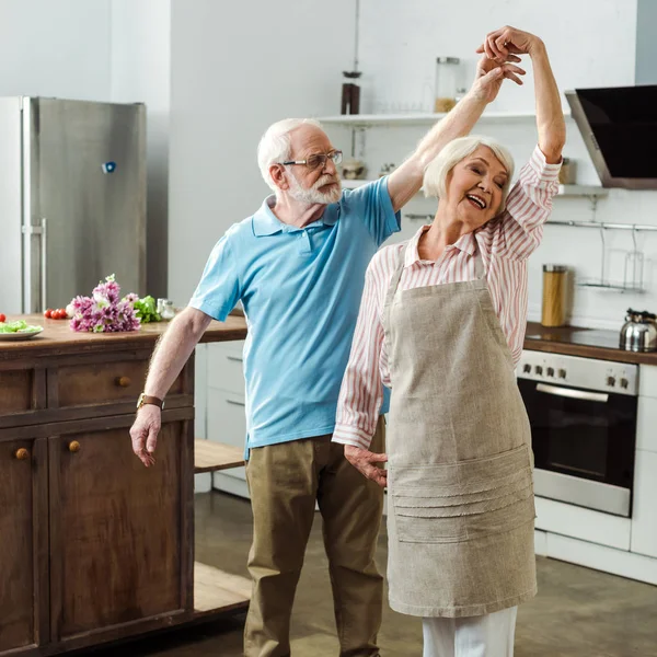 老人和笑着的妻子一起在厨房桌上用蔬菜和花束跳舞 — 图库照片