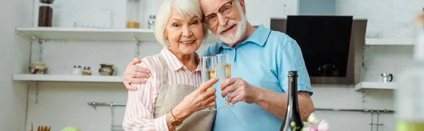 Panoramatický Záběr Seniorského Páru Přípitek Šampaňským Při Pohledu Kameru Kuchyni — Stock fotografie