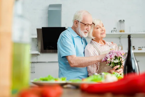 Selective Focus Smiling Senior Couple Bouquet Champagne Hugging Vegetables Kitchen — Stock Photo, Image