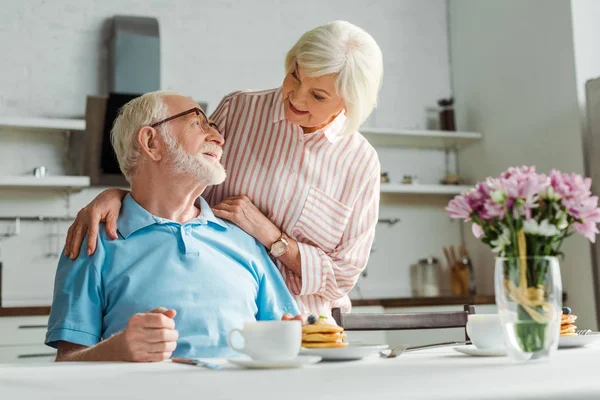 Selective Focus Senior Woman Hugging Smiling Husband Coffee Pancakes Table — Stock Photo, Image