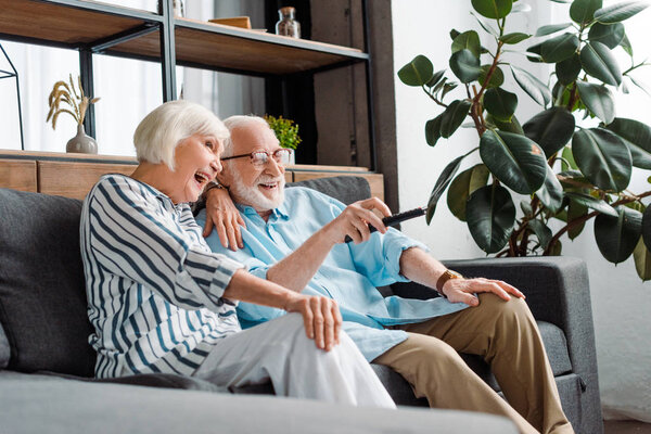 Selective focus of cheerful senior couple watching tv on couch in living room