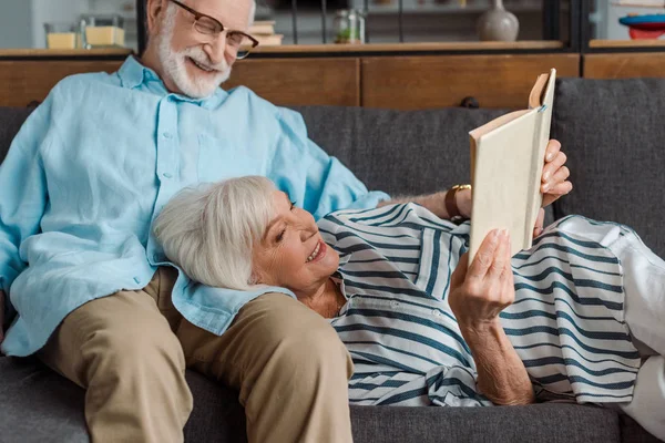 Smiling Woman Reading Book While Lying Husband Couch — Stock Photo, Image