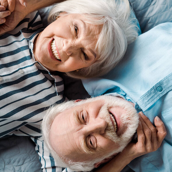 Top view of elderly couple smiling at camera while lying on bed