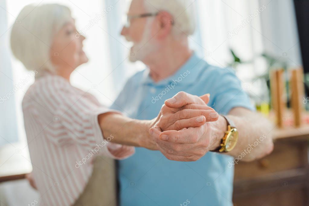 Selective focus of senior couple holding hands while dancing in kitchen