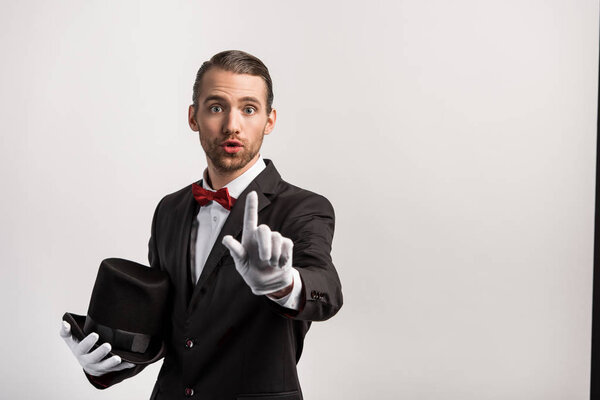 emotional magician in gloves pointing up, isolated on grey