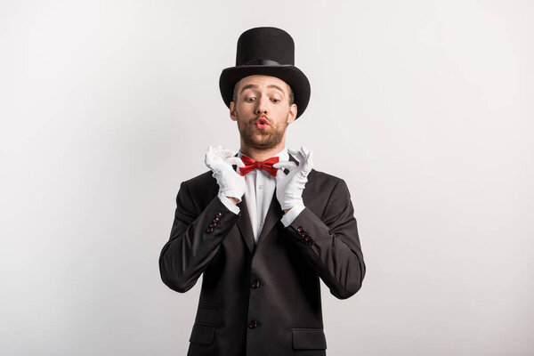 emotional magician adjusting red bow tie, isolated on grey