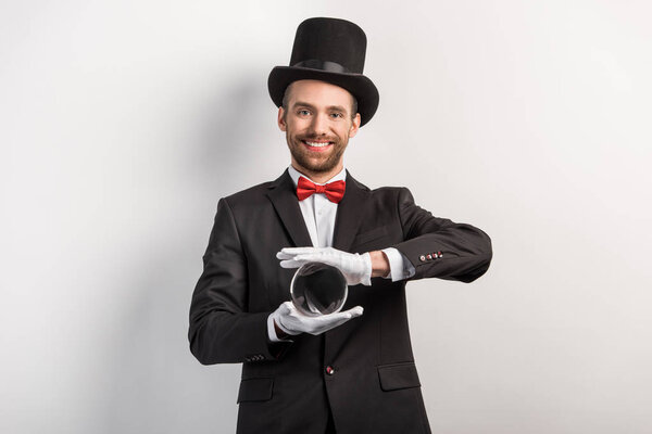 happy professional magician holding magic ball, on grey