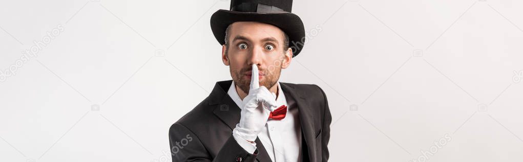 panoramic shot of emotional magician in gloves showing silence symbol, isolated on grey