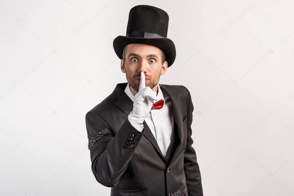 surprised magician in gloves showing silence symbol, isolated on grey