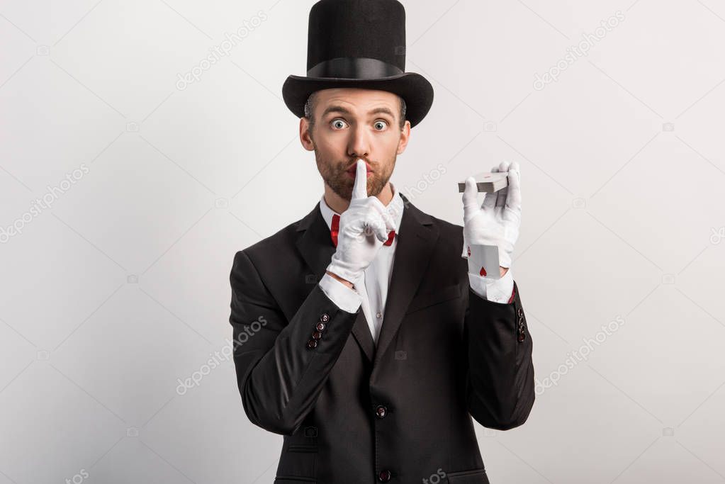 magician holding playing cards and showing silence symbol, isolated on grey
