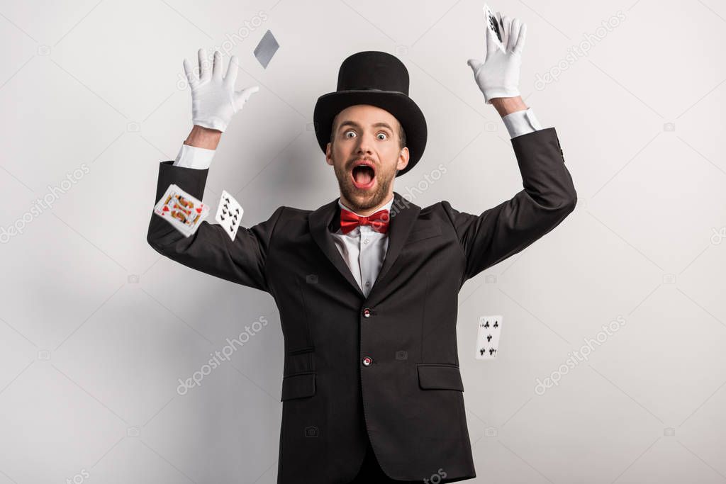 surprised magician throwing playing cards, on grey